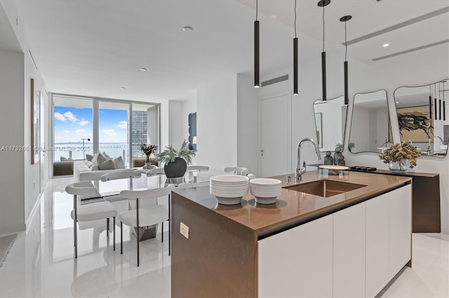 kitchen with a center island with sink, modern cabinets, white cabinetry, pendant lighting, and a sink