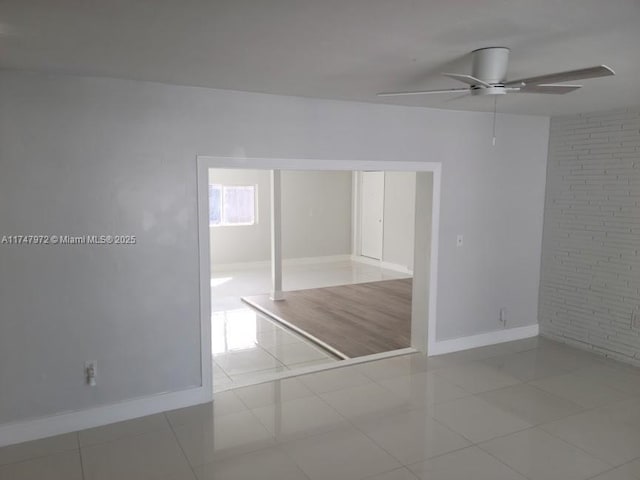 unfurnished room featuring a ceiling fan, baseboards, brick wall, and light tile patterned floors