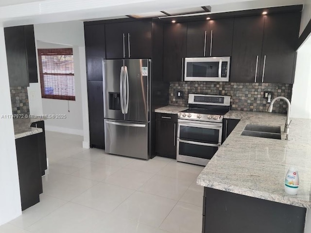 kitchen featuring light tile patterned floors, decorative backsplash, appliances with stainless steel finishes, a sink, and dark cabinets