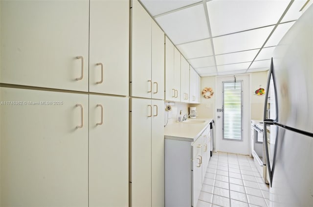 kitchen with a drop ceiling, appliances with stainless steel finishes, light countertops, white cabinetry, and a sink