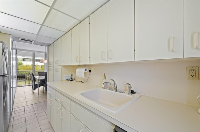 kitchen featuring a drop ceiling, a sink, white cabinets, light countertops, and freestanding refrigerator