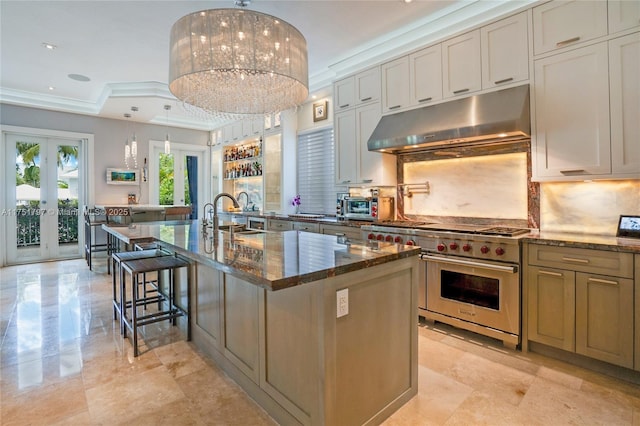 kitchen with under cabinet range hood, a center island with sink, dark stone counters, and range with two ovens