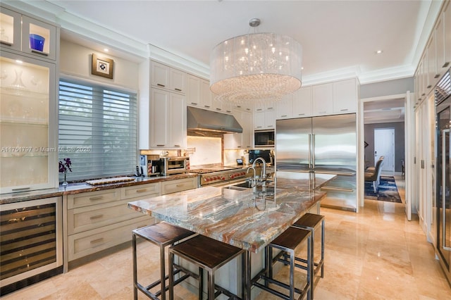 kitchen with built in appliances, wine cooler, under cabinet range hood, a breakfast bar, and a sink