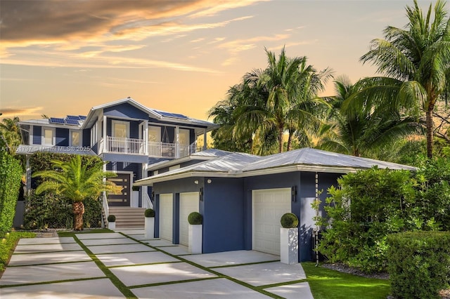 view of front of house featuring stucco siding, roof mounted solar panels, metal roof, a balcony, and driveway