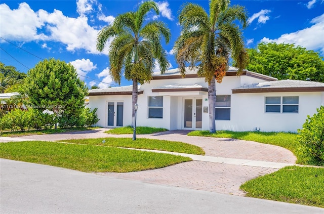 view of front facade featuring decorative driveway, french doors, a front lawn, and stucco siding