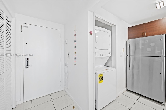 laundry area featuring visible vents, baseboards, stacked washer and dryer, laundry area, and light tile patterned flooring