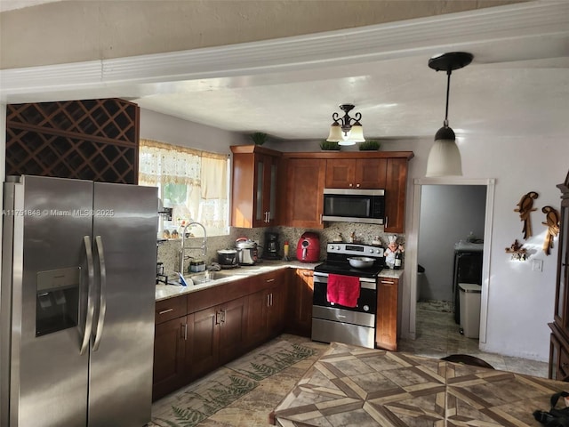 kitchen featuring decorative light fixtures, stainless steel appliances, tasteful backsplash, light countertops, and a sink