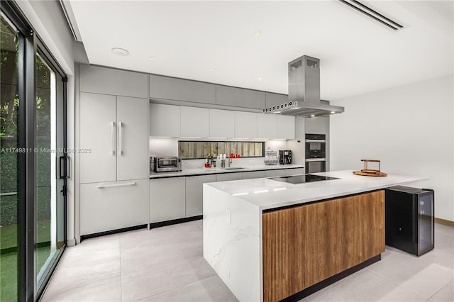 kitchen with stainless steel double oven, black electric cooktop, island range hood, a sink, and modern cabinets