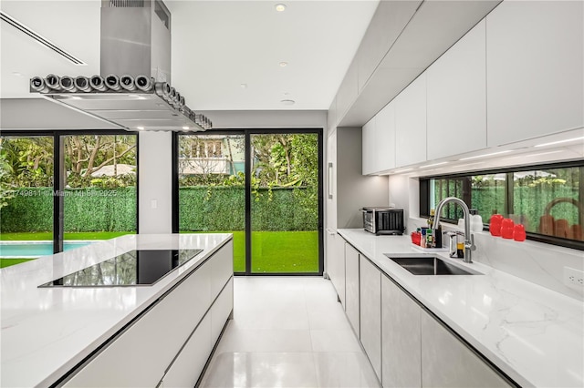 kitchen with light stone counters, extractor fan, a sink, white cabinetry, and a healthy amount of sunlight