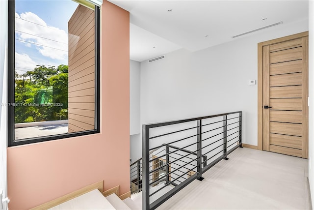 hall with baseboards, visible vents, concrete flooring, and an upstairs landing