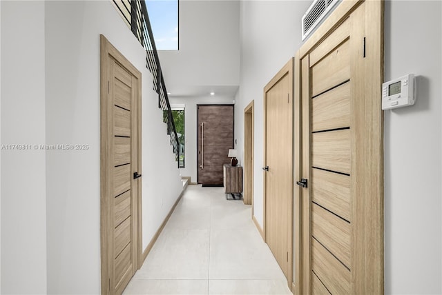 corridor featuring visible vents, a high ceiling, light tile patterned flooring, baseboards, and stairs