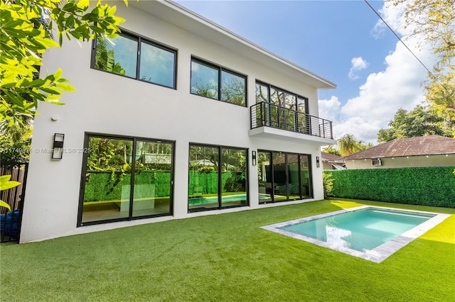 back of house featuring a lawn, a balcony, and stucco siding