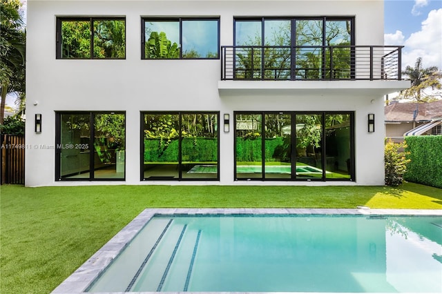 back of property with a balcony, a lawn, and stucco siding