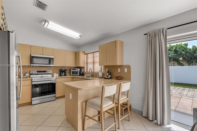15010 SW 178th Ter, Miami, FL 33187 - kitchen featuring a breakfast bar area, a peninsula, light countertops, appliances with stainless steel finishes, and light brown cabinetry