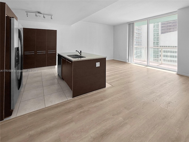 kitchen featuring a sink, light countertops, stainless steel refrigerator with ice dispenser, light wood finished floors, and a center island with sink