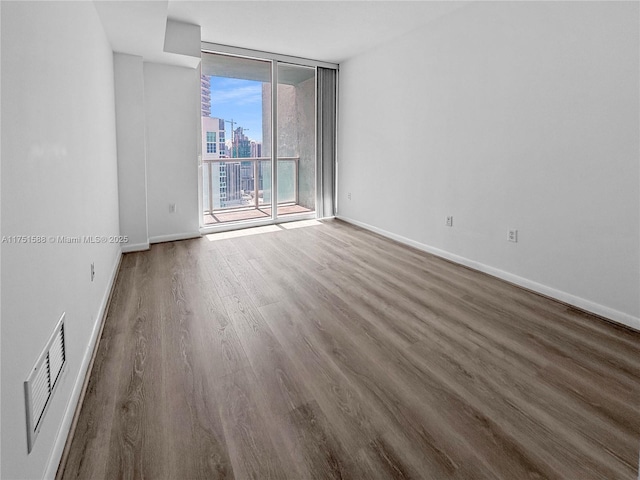 unfurnished room with baseboards, floor to ceiling windows, dark wood-style flooring, and a city view