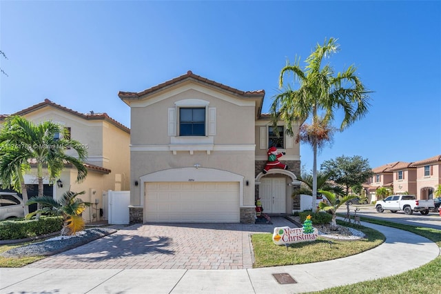 mediterranean / spanish-style house with a garage, a tile roof, stone siding, decorative driveway, and stucco siding