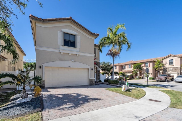 mediterranean / spanish-style house featuring an attached garage, a tile roof, decorative driveway, a residential view, and stucco siding