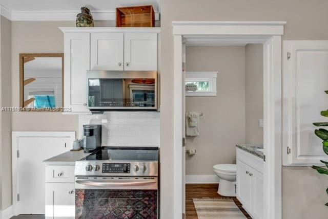 kitchen featuring baseboards, white cabinets, appliances with stainless steel finishes, ornamental molding, and wood finished floors