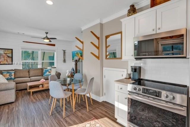 kitchen featuring dark wood finished floors, stainless steel appliances, ornamental molding, open floor plan, and white cabinets