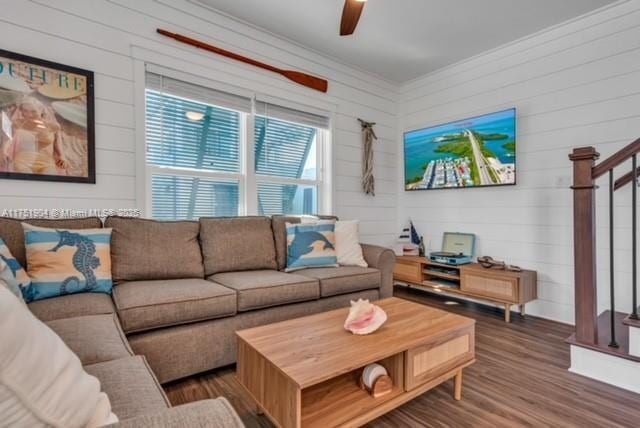 living area with ceiling fan, stairs, ornamental molding, and dark wood-type flooring