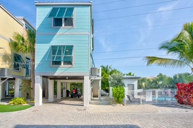 view of front of home with cooling unit, decorative driveway, fence, and a carport