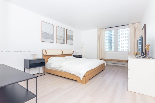 bedroom with light wood-type flooring and a baseboard heating unit