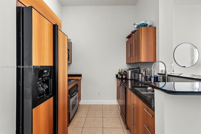 kitchen featuring dark stone counters, light tile patterned flooring, stainless steel oven, refrigerator with ice dispenser, and brown cabinets