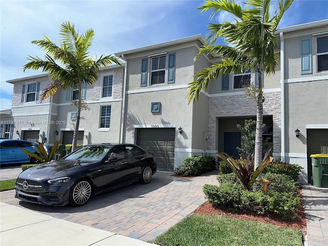 view of property with an attached garage, stone siding, decorative driveway, and stucco siding