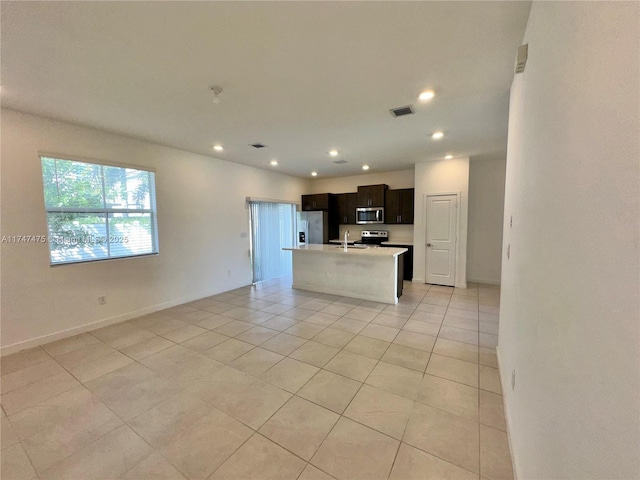 kitchen featuring stainless steel appliances, visible vents, open floor plan, light countertops, and an island with sink