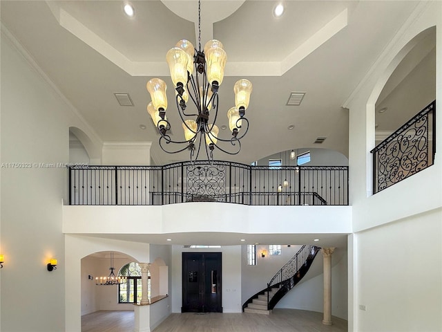 staircase with arched walkways, a notable chandelier, visible vents, a raised ceiling, and elevator