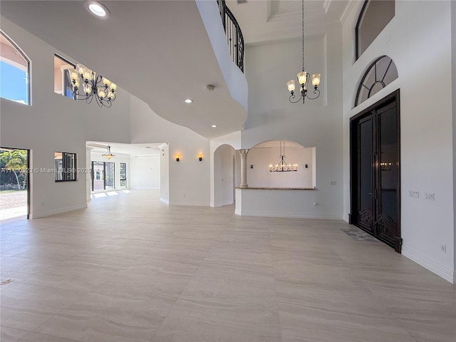 unfurnished living room with a towering ceiling, an inviting chandelier, baseboards, and arched walkways