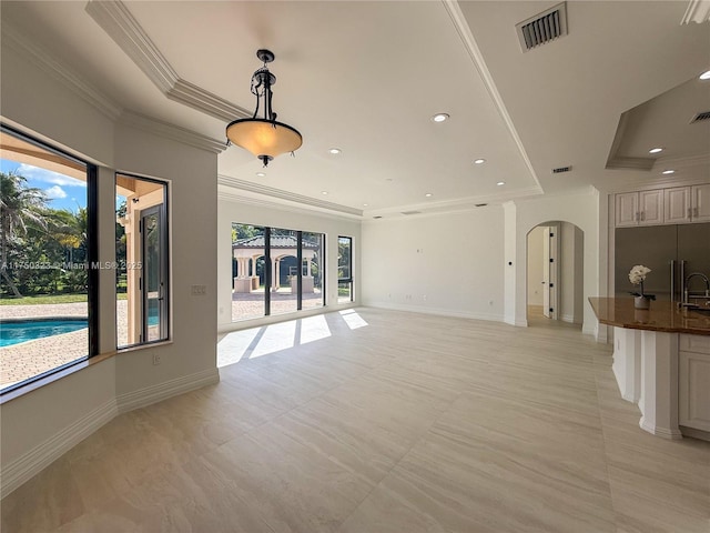 unfurnished living room with arched walkways, a tray ceiling, visible vents, and baseboards