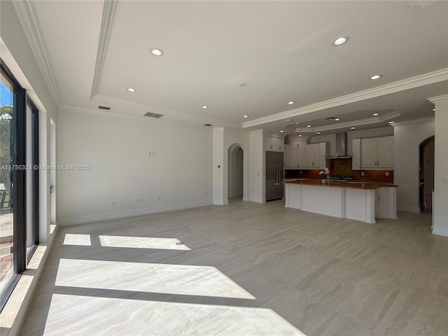 unfurnished living room featuring arched walkways, a tray ceiling, baseboards, and recessed lighting