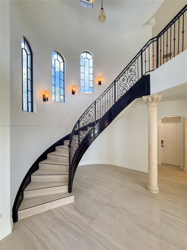 stairway with a towering ceiling, ornate columns, and baseboards