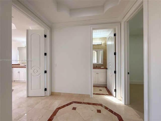 corridor featuring a tray ceiling, a sink, crown molding, and baseboards