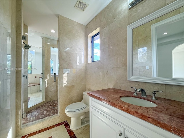 bathroom with a stall shower, visible vents, toilet, vanity, and tile walls