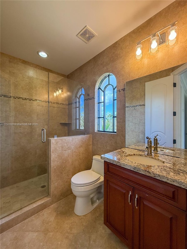 bathroom featuring toilet, vanity, visible vents, tile walls, and a stall shower