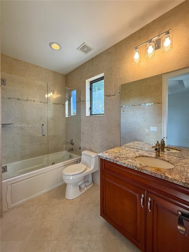 bathroom featuring visible vents, toilet, shower / bath combination with glass door, vanity, and tile walls