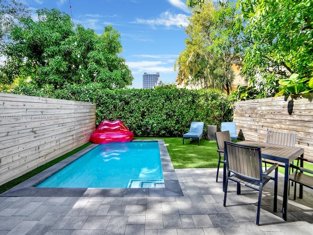 view of pool with outdoor dining space, a fenced backyard, a patio, and a view of city