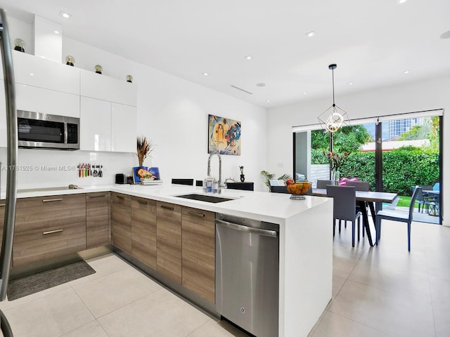 kitchen with light countertops, appliances with stainless steel finishes, a sink, modern cabinets, and a peninsula