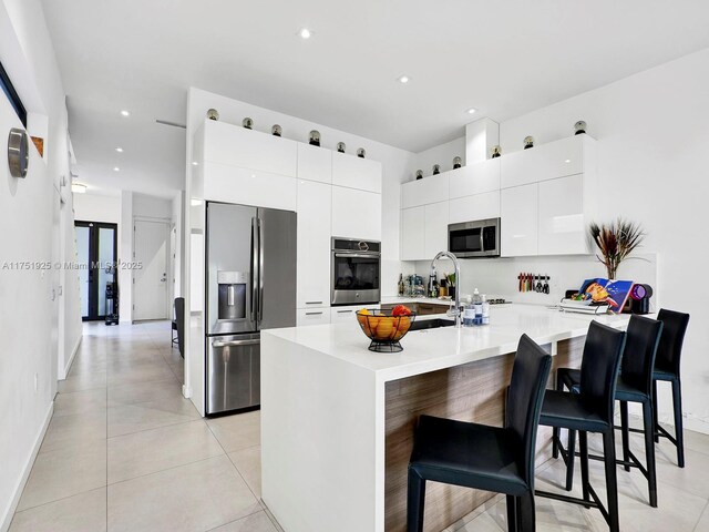 kitchen with a kitchen breakfast bar, white cabinets, light countertops, appliances with stainless steel finishes, and modern cabinets