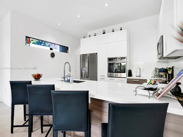 kitchen featuring a breakfast bar area, a sink, light countertops, appliances with stainless steel finishes, and modern cabinets