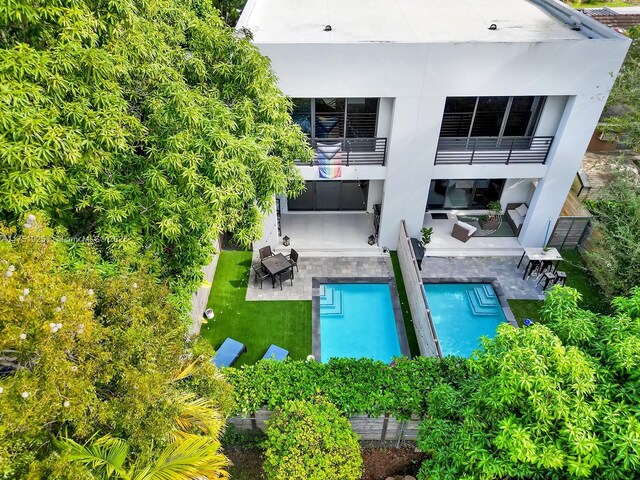 back of property featuring a yard, a patio area, a balcony, and an outdoor pool