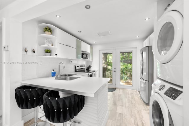 kitchen with decorative backsplash, white cabinets, stacked washer and clothes dryer, appliances with stainless steel finishes, and a sink