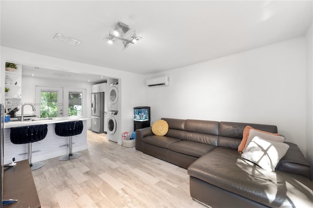 living room featuring a wall unit AC, stacked washing maching and dryer, light wood-type flooring, and french doors