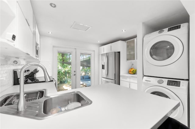 kitchen with a sink, white cabinetry, light countertops, appliances with stainless steel finishes, and stacked washing maching and dryer