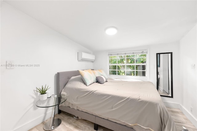 bedroom with light wood-type flooring, a wall mounted air conditioner, and baseboards