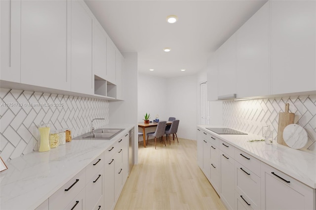 kitchen with black electric stovetop, light stone countertops, white cabinets, and a sink