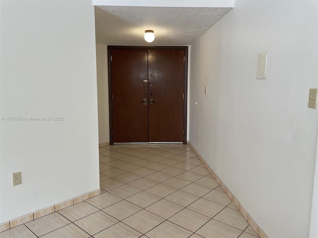 hall featuring a textured ceiling, baseboards, and light tile patterned floors